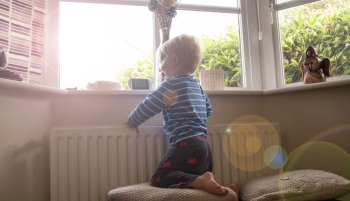 Enfant se tenant près d'un radiateur et d'une fenêtre